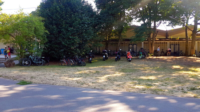 „Wild“ abgestellte Fahrräder und Motorroller neben dem Freibadeingang.